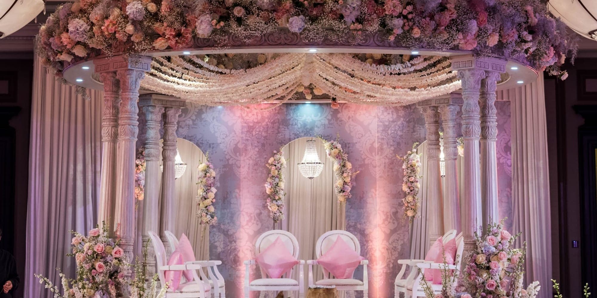 Round floral canopy mandap lit in pink and lilac with pink ceremony chairs