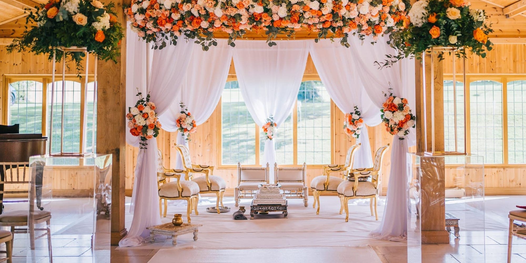 Timber hall with a white draped mandap topped with orange and cream flowers