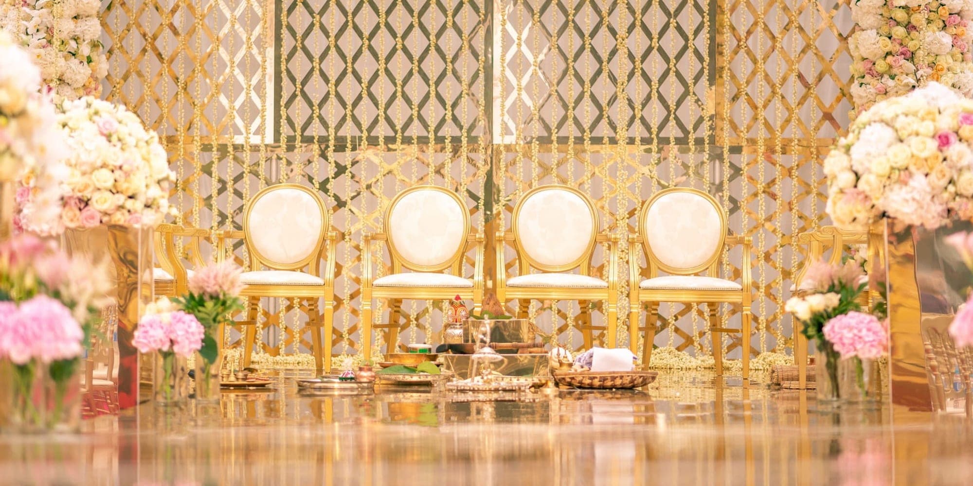 Gold lattice backdrop with cream chairs and flowers on a mirrored floor
