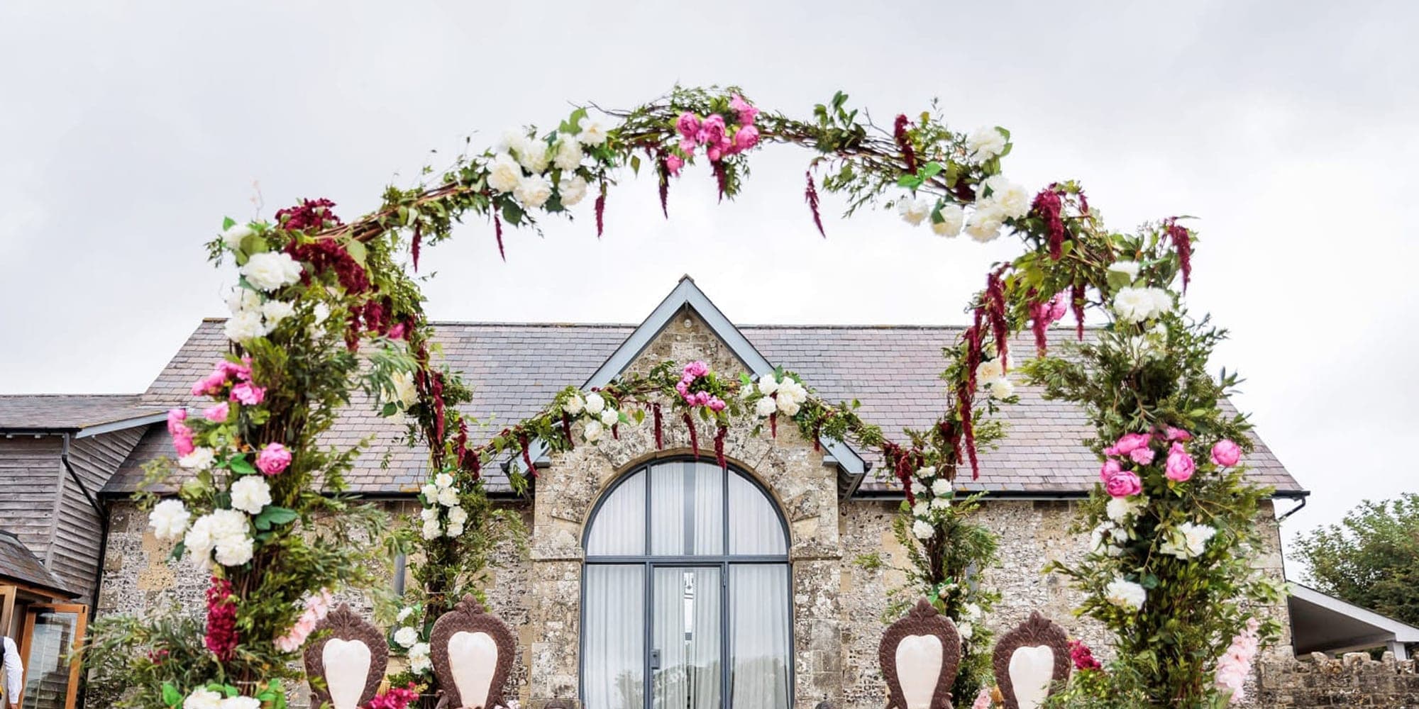 Floral ring arch mandap with carved seats in front of a stone building