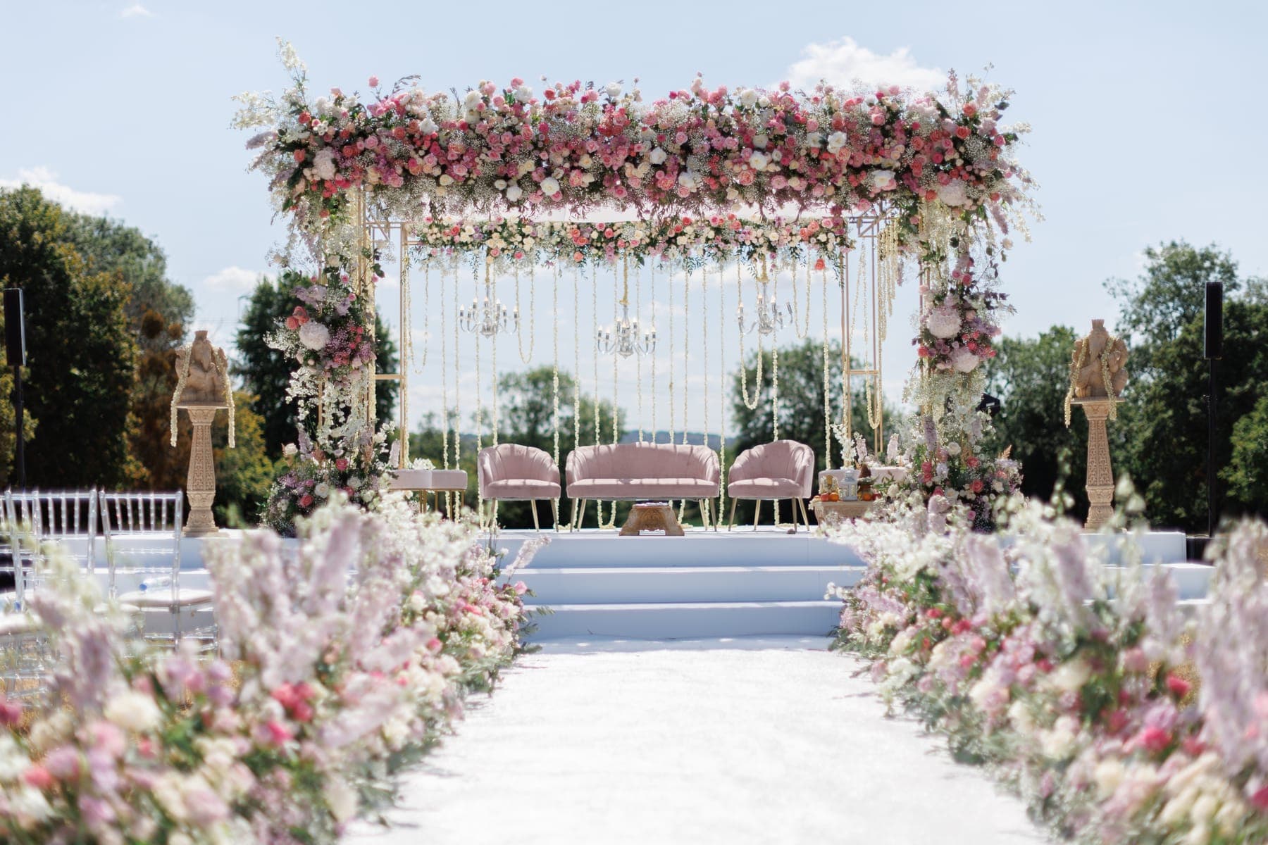 Pink floral square frame with chandeliers and a blush sofa, seen down a flower-lined white aisle