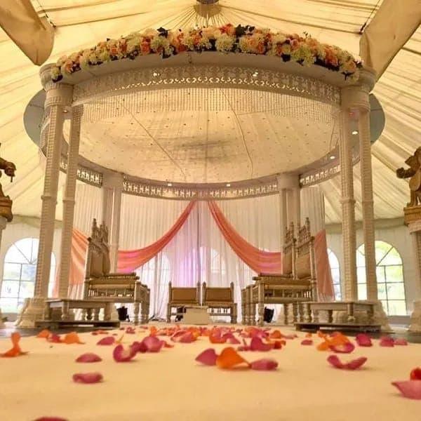 Round carved canopy with peach flowers and drapes inside a cream marquee