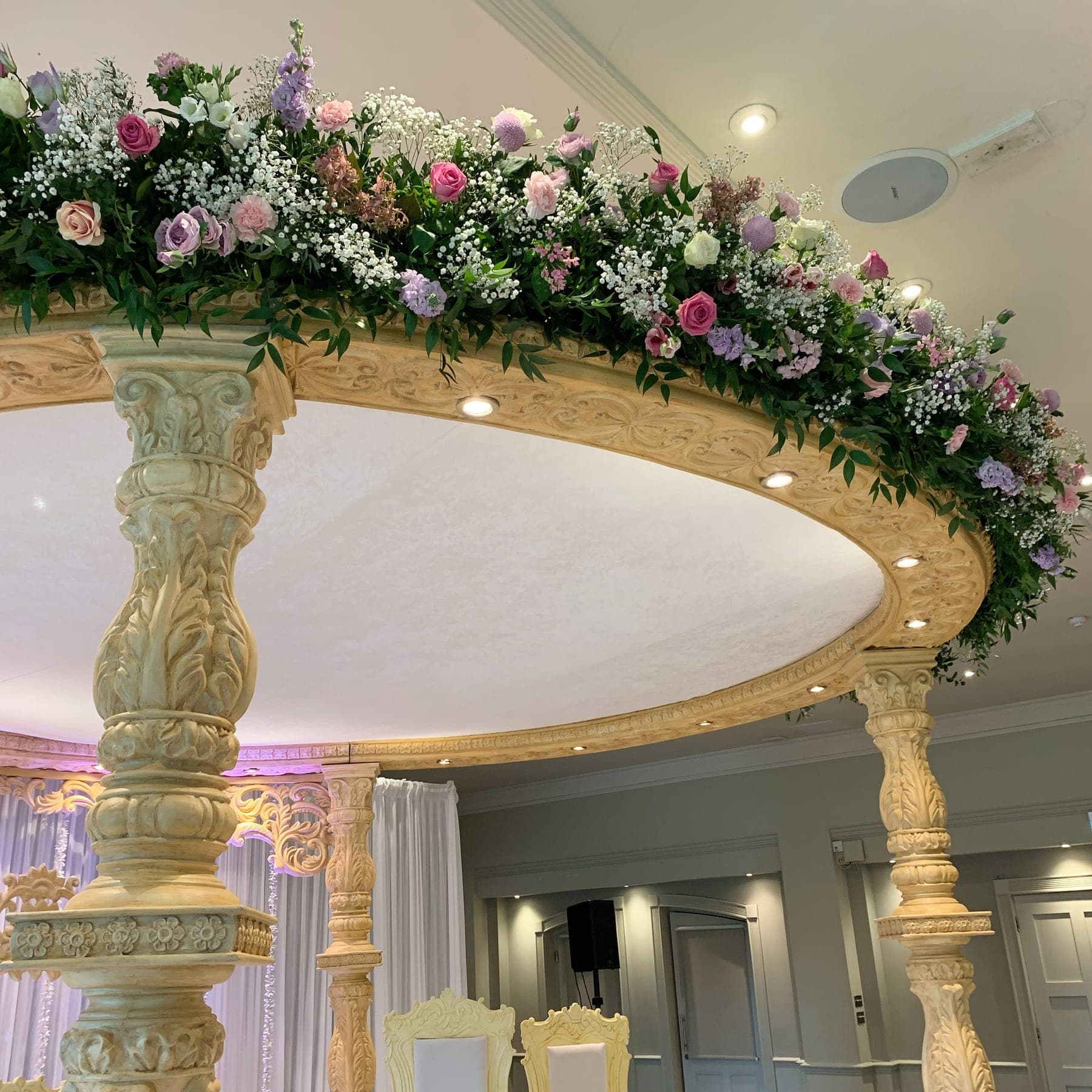 Oval cream carved canopy edged with pink and lilac flowers above ivory chairs
