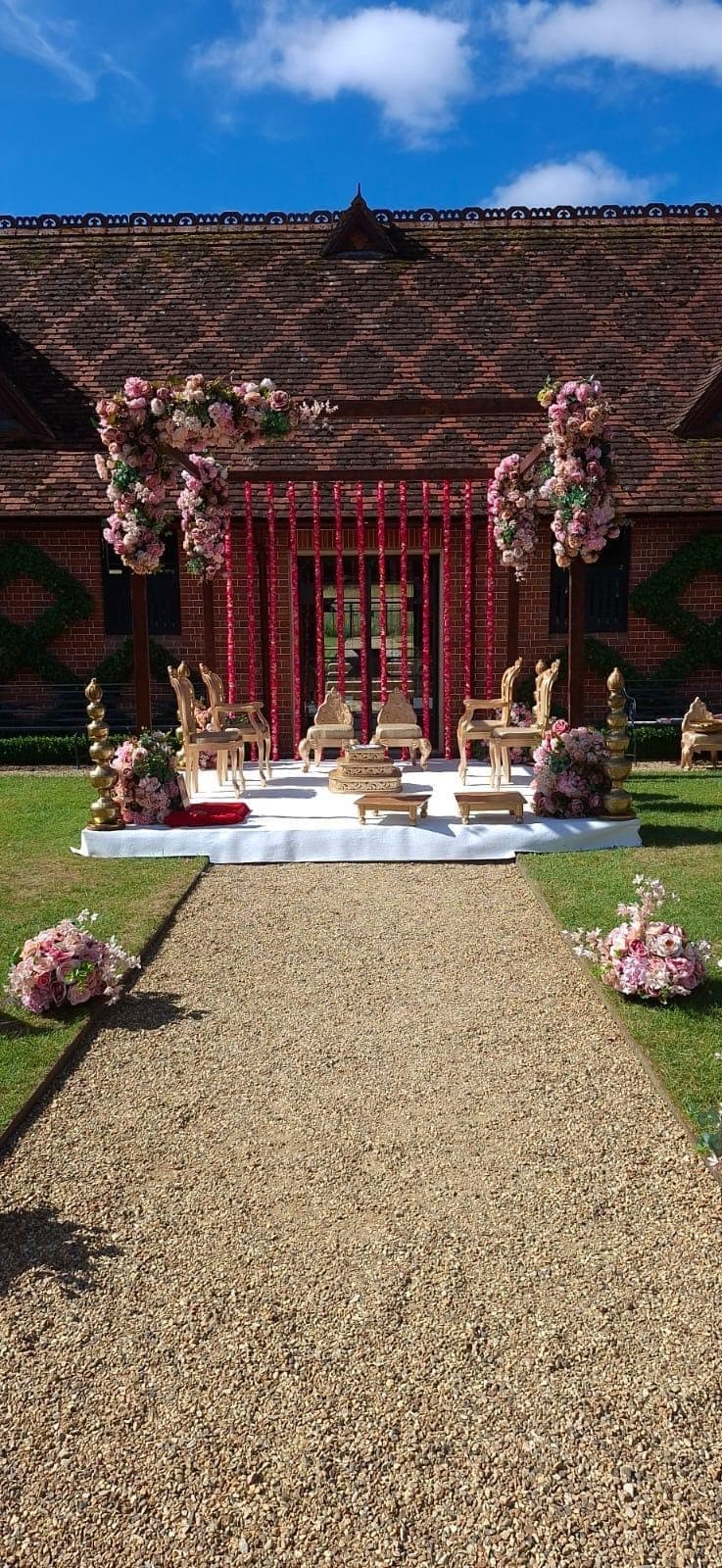 Red framed mandap at the end of a gravel path in a brick courtyard