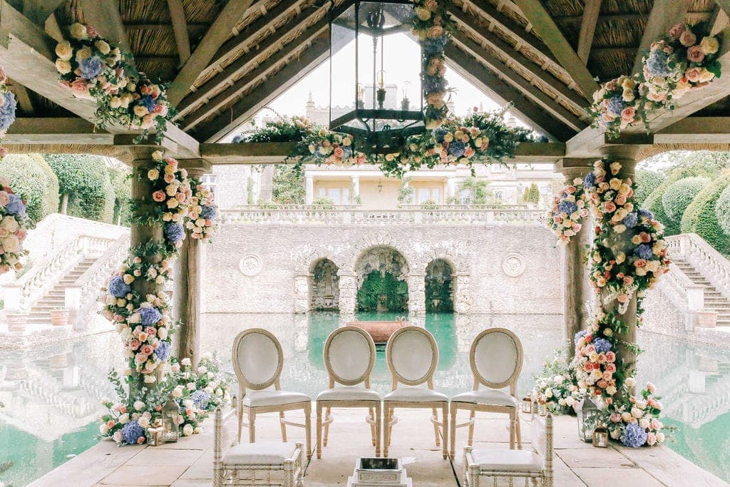 Cream round-backed chairs inside a thatched gazebo with blue and peach flower-wrapped posts