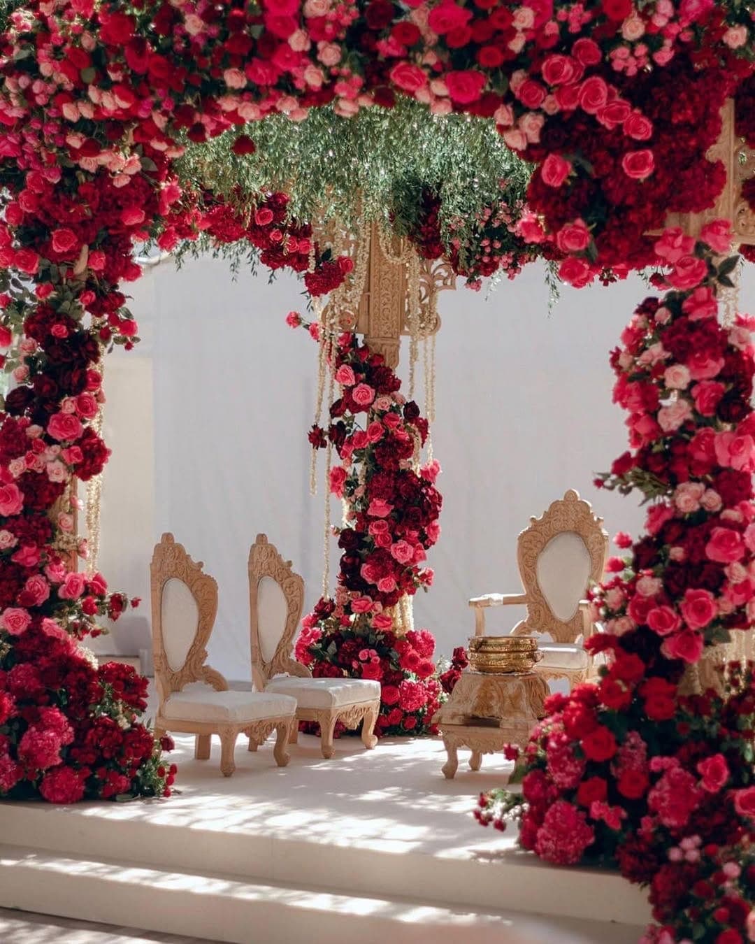 Close view of rose-covered posts and carved cream chairs beneath a hanging green canopy
