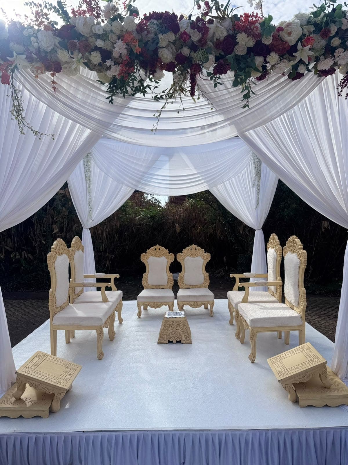 White draped canopy with a red and pink floral band at the end of a long white garden aisle