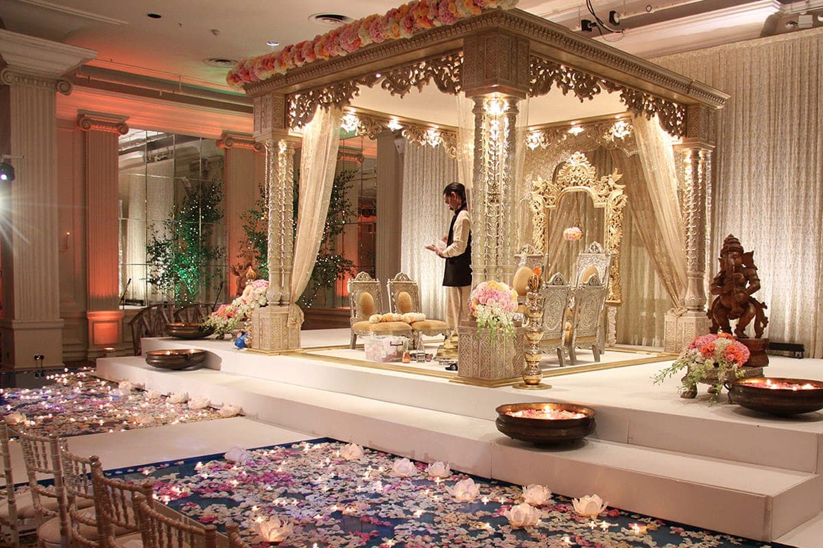 Gold fretwork mandap on a raised podium with petal-strewn aisle and brass bowls