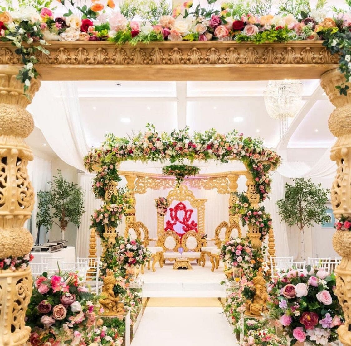 Gold carved mandap wrapped in pink and cream flowers with red Ganesh backdrop