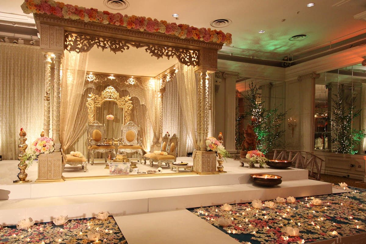Gold carved frame mandap with peach flower garland and gilded throne
