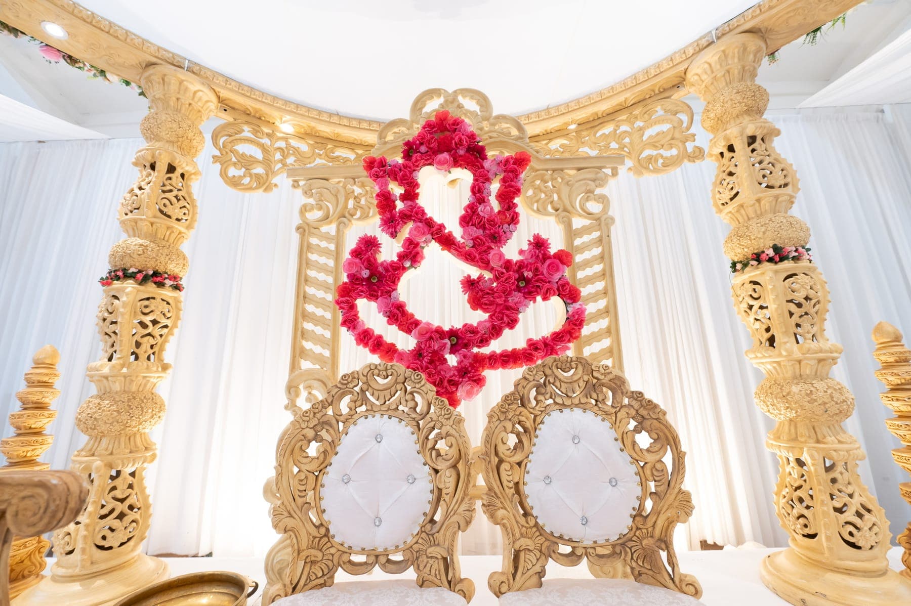 Close view of gold carved pillars and ornate chairs beneath a hot pink rose Ganesh outline