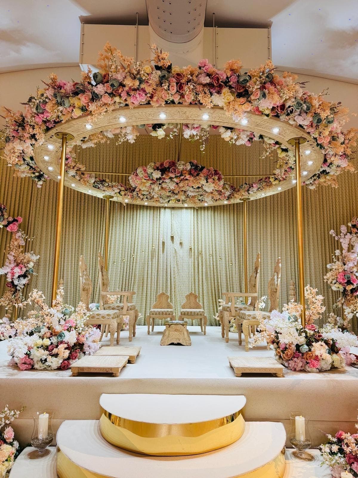 Round floral canopy over a white stage with gold curtains and a gold half-moon step