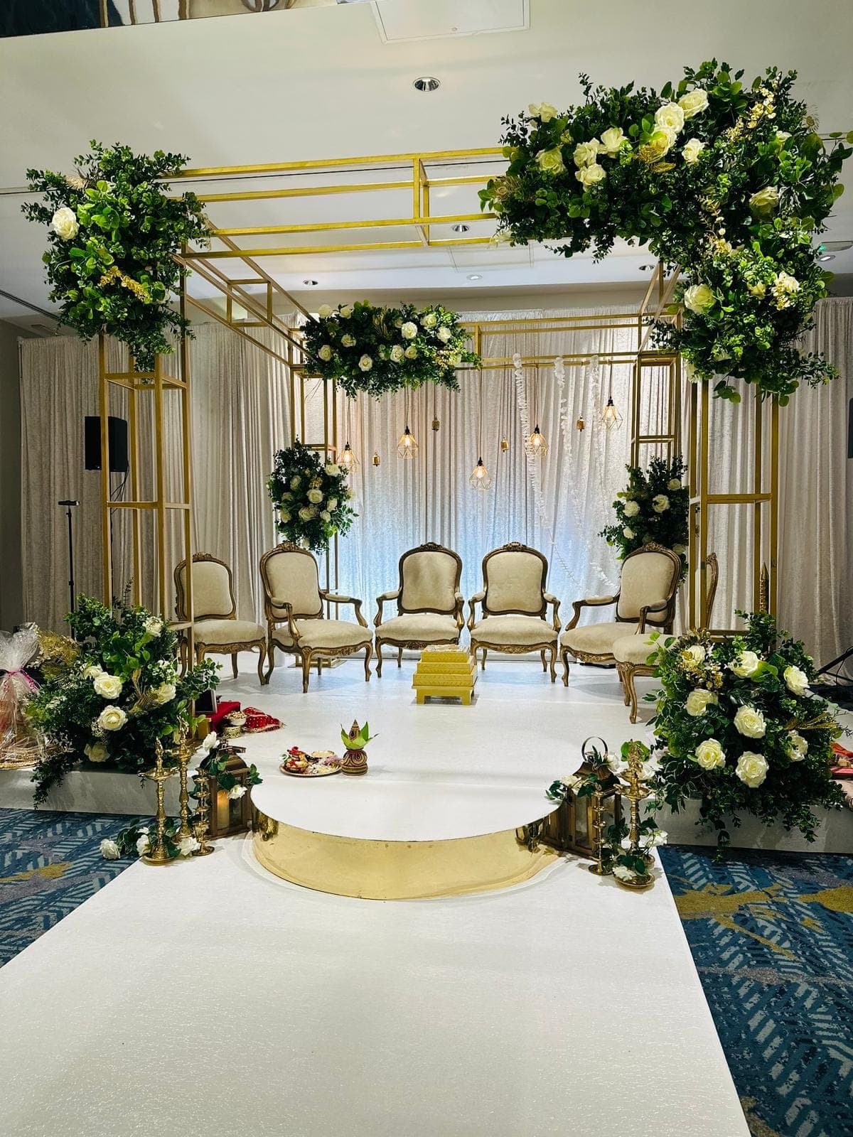 Gold frame mandap with white roses and greenery in a hotel room