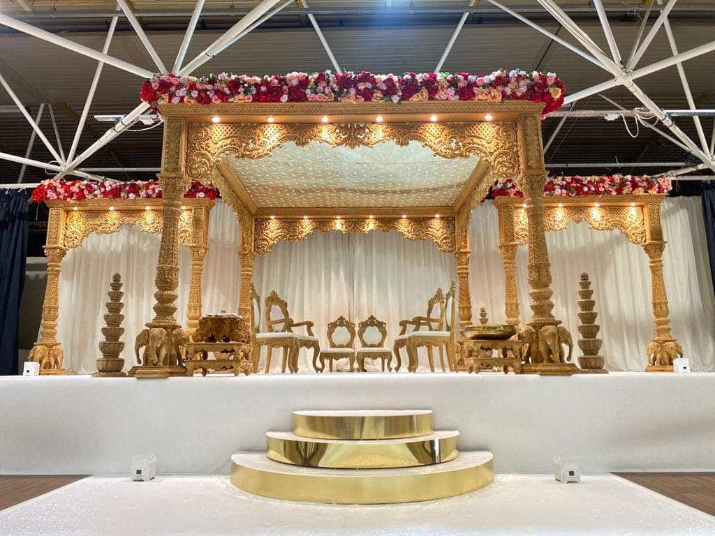 Gold carved stage mandap with elephants and red flower crowns in a large hall