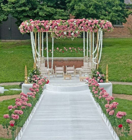 Pink rose-topped mandap with white garlands on a garden lawn