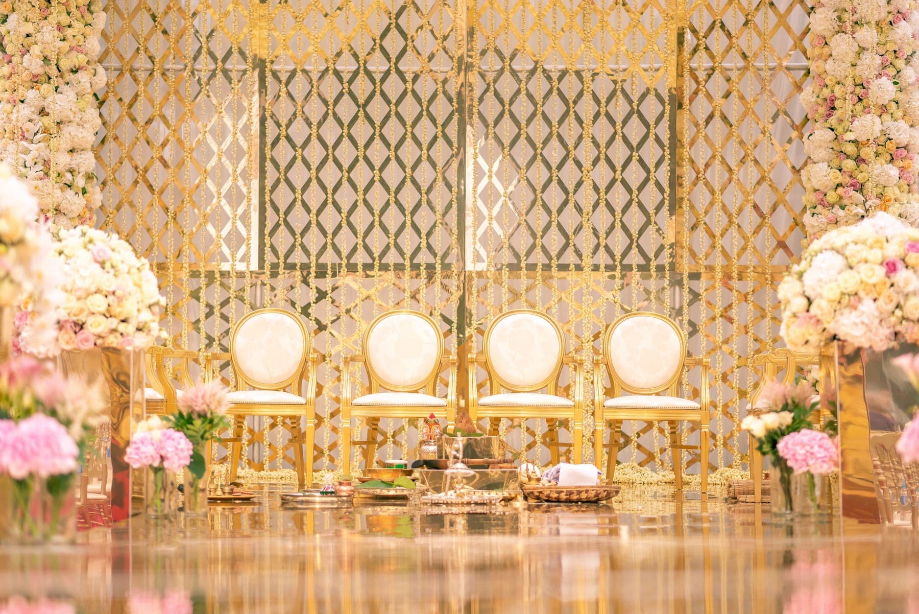 Four gold armchairs with ivory backs before a gold lattice backdrop and tall cream rose columns