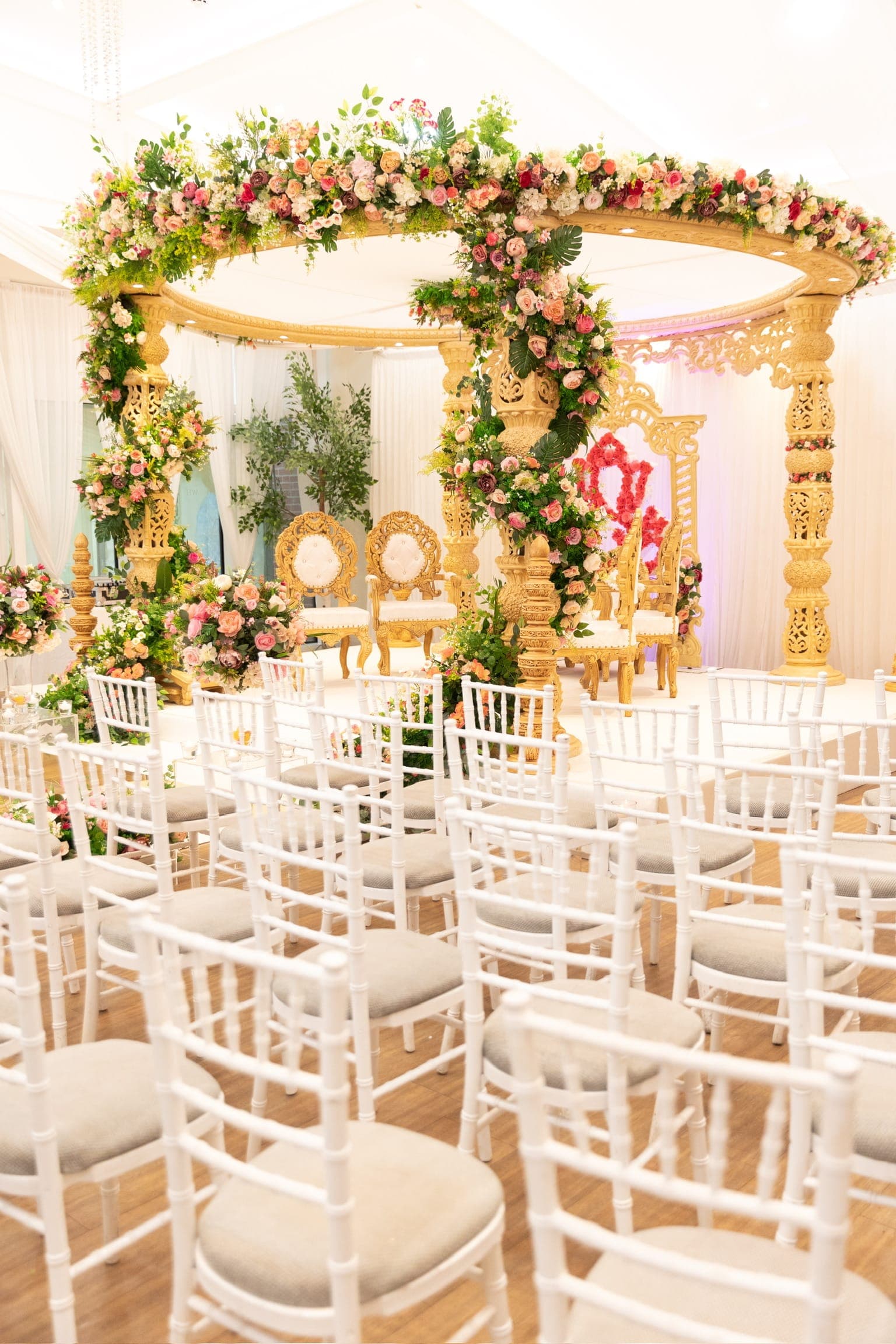 Gold round mandap wreathed in pink roses, ferns and tropical leaves