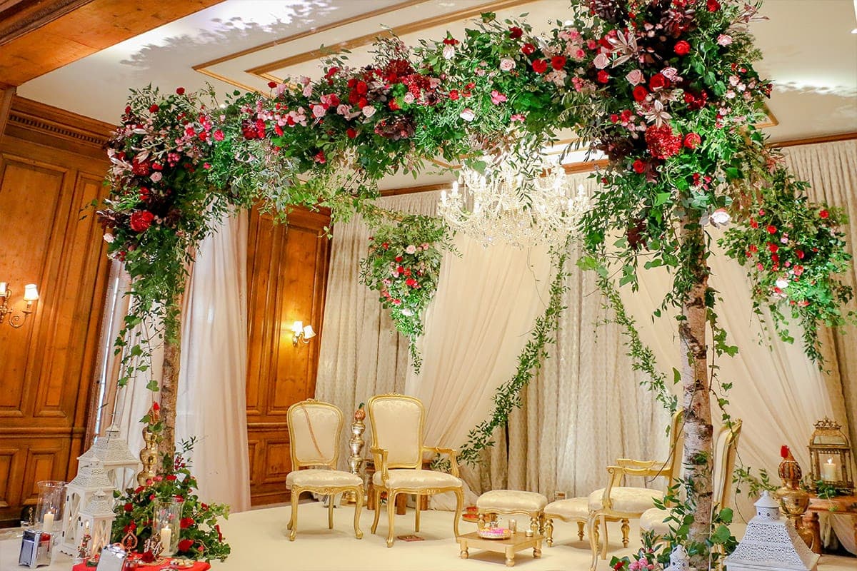 Birch frame mandap with red and pink roses and foliage under a chandelier