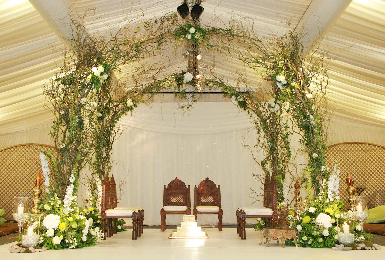 Twisted twig arches with ivy and white roses over two dark chairs in a marquee