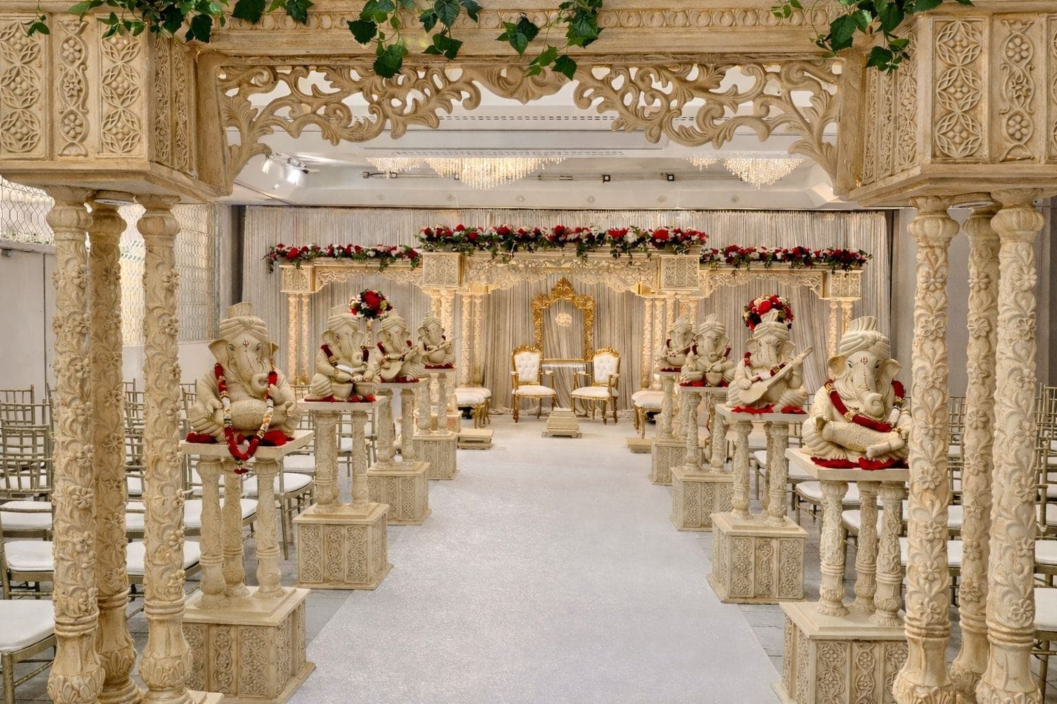 Ivory carved entrance pillars with Ganesh statues leading to a gilded mandap
