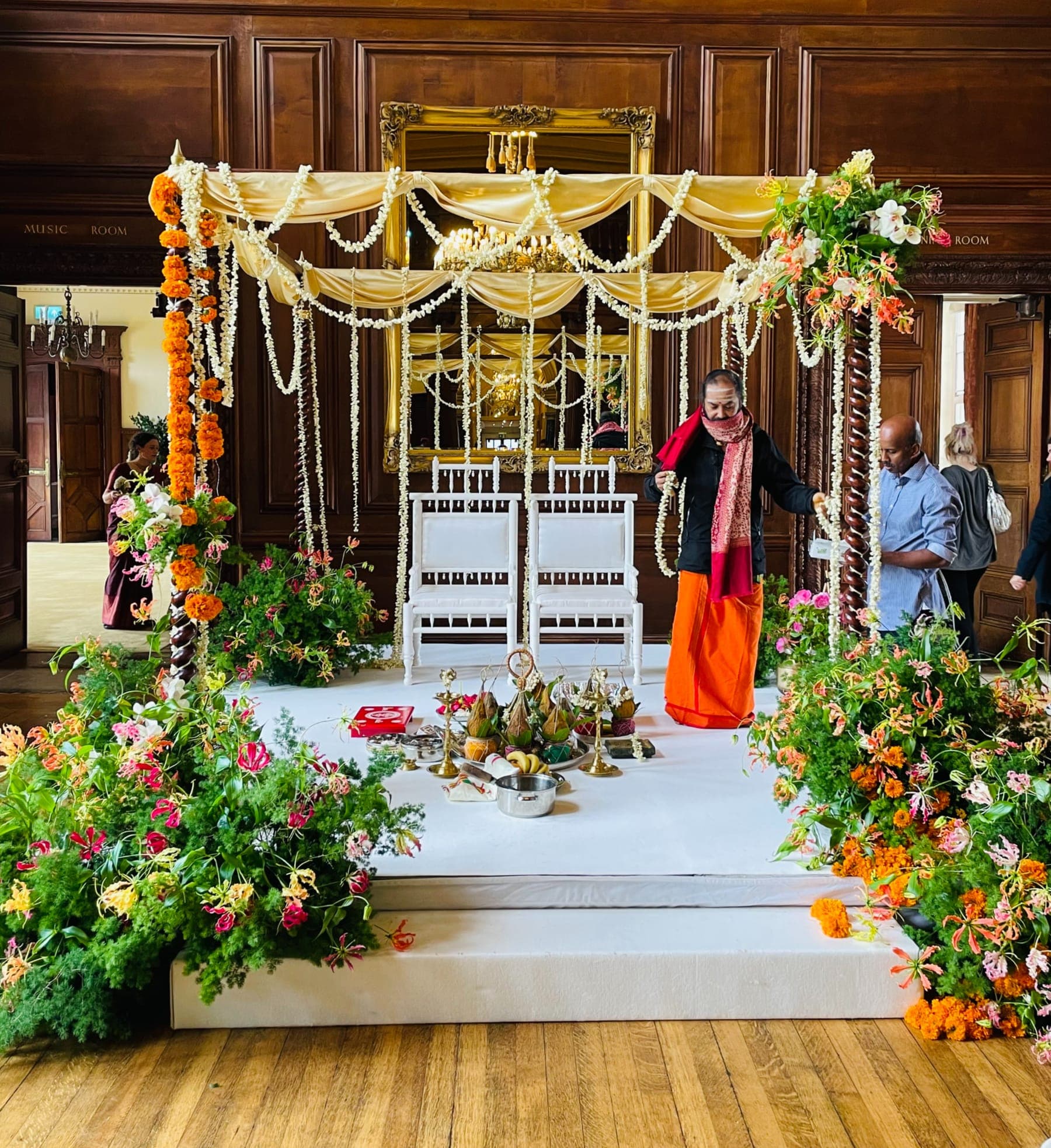 Frame with gold drape, white garlands and marigold stack in a wood-panelled hall