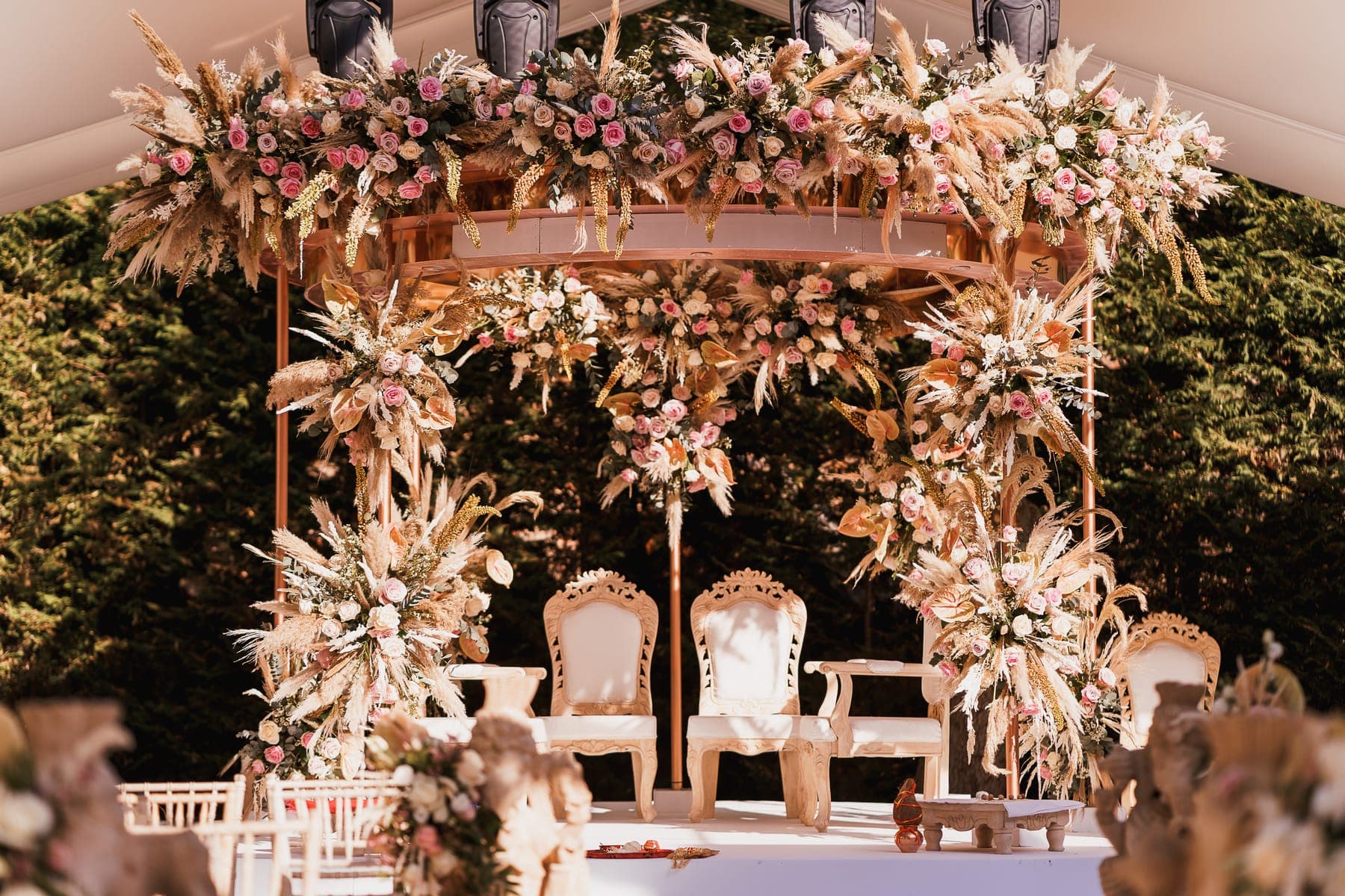 Rose gold round canopy with pampas grass, blush roses and carved cream chairs