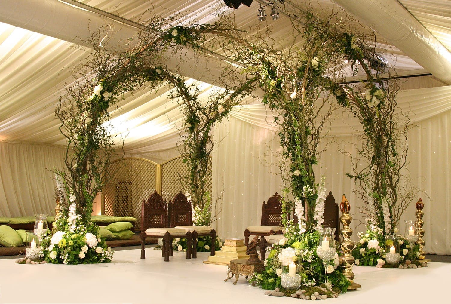 Crossed ivy and rose arches with carved chairs and green cushions in a marquee
