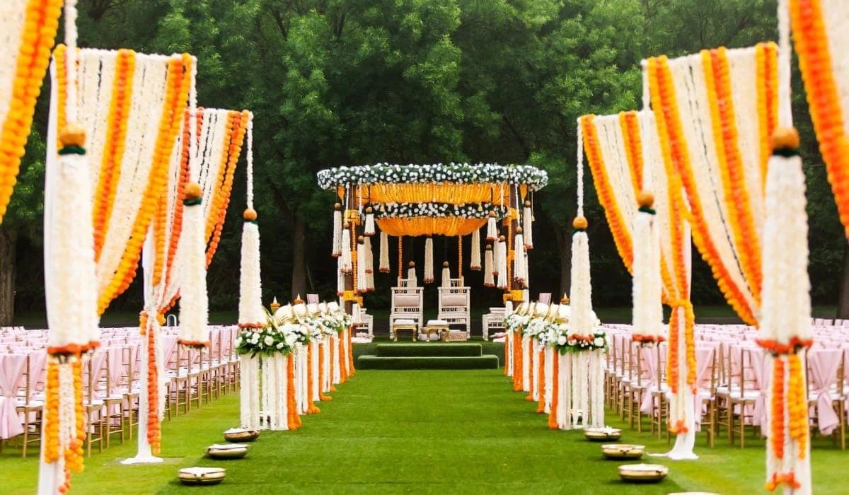 Orange and white garland columns line a lawn aisle leading to a small canopy