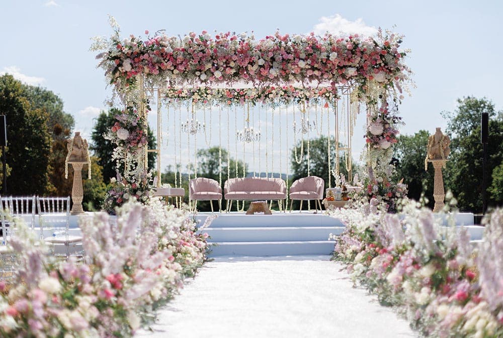 Gold frame with pink and white roses, chandeliers and blush sofa beside a white aisle