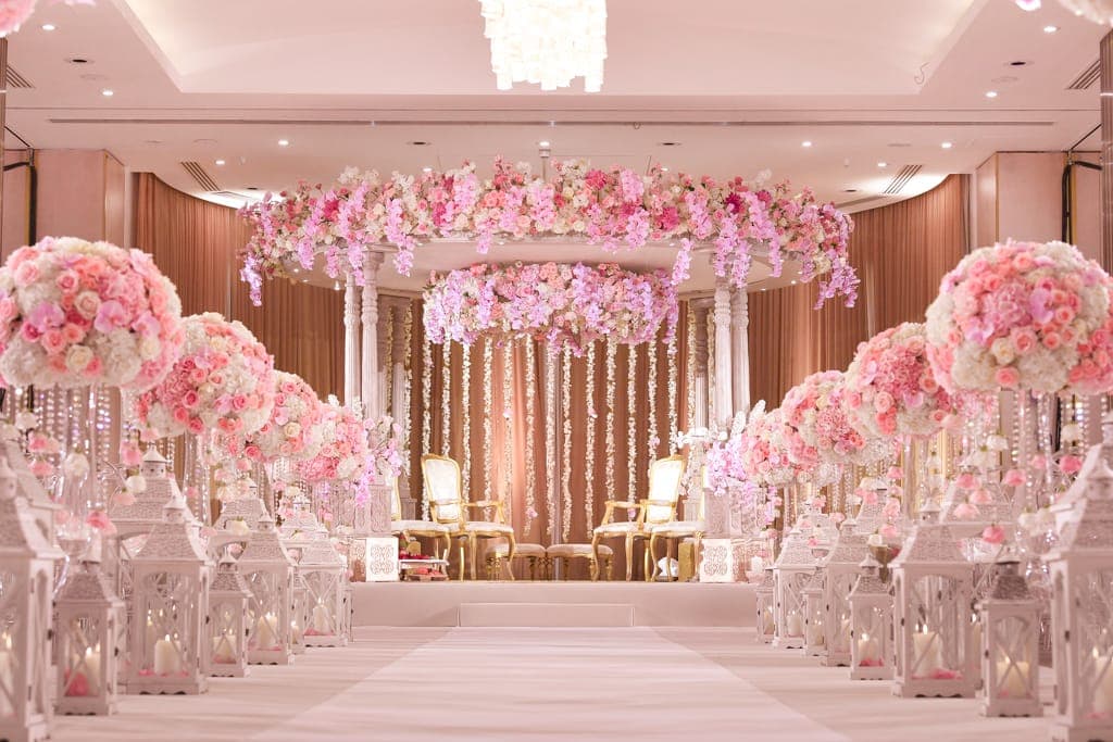 Pink orchid canopy mandap above a white lantern aisle in a peach-draped hall