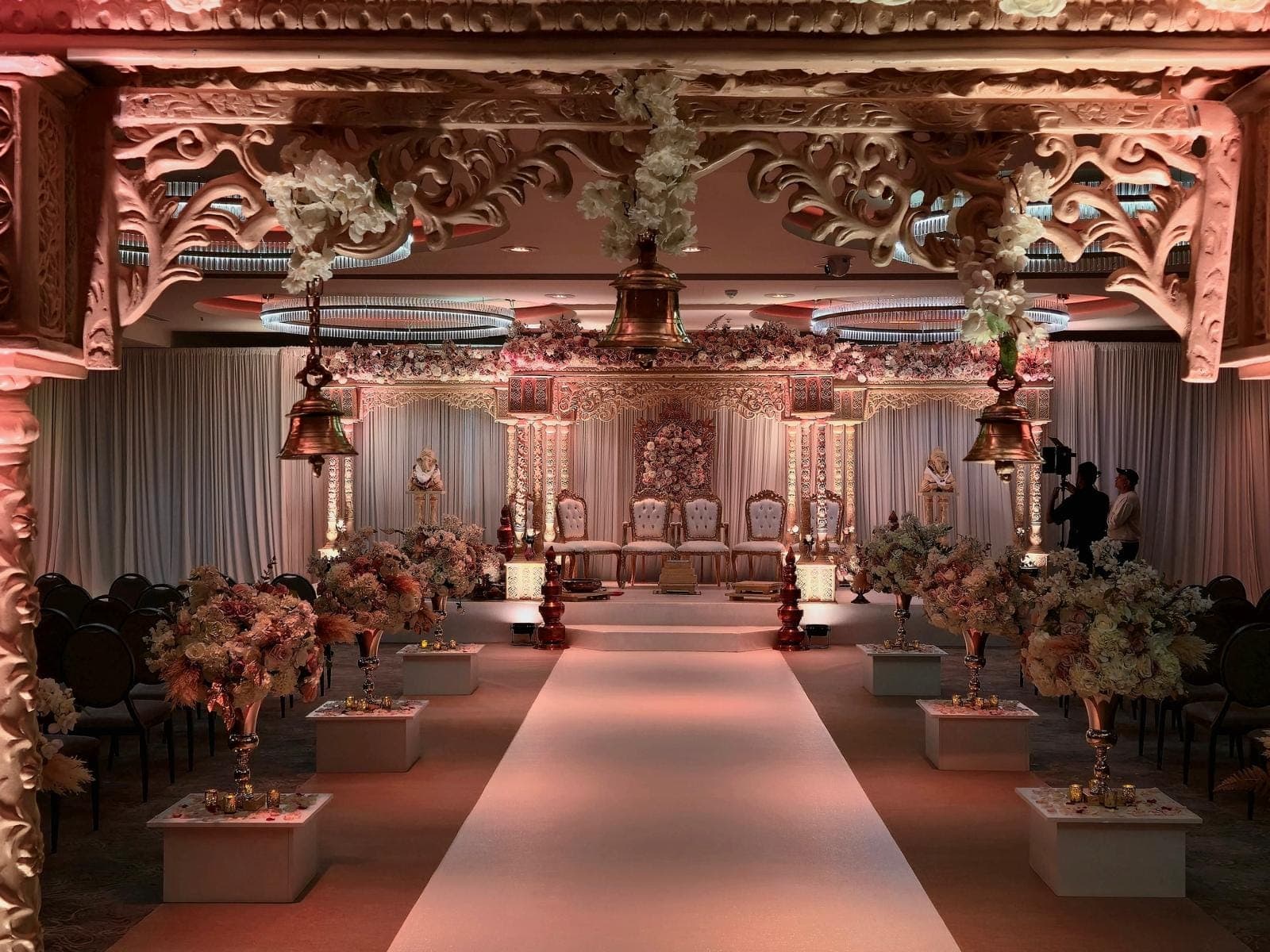 Carved pink-cream entrance frame with bells overlooking a long aisle and mandap