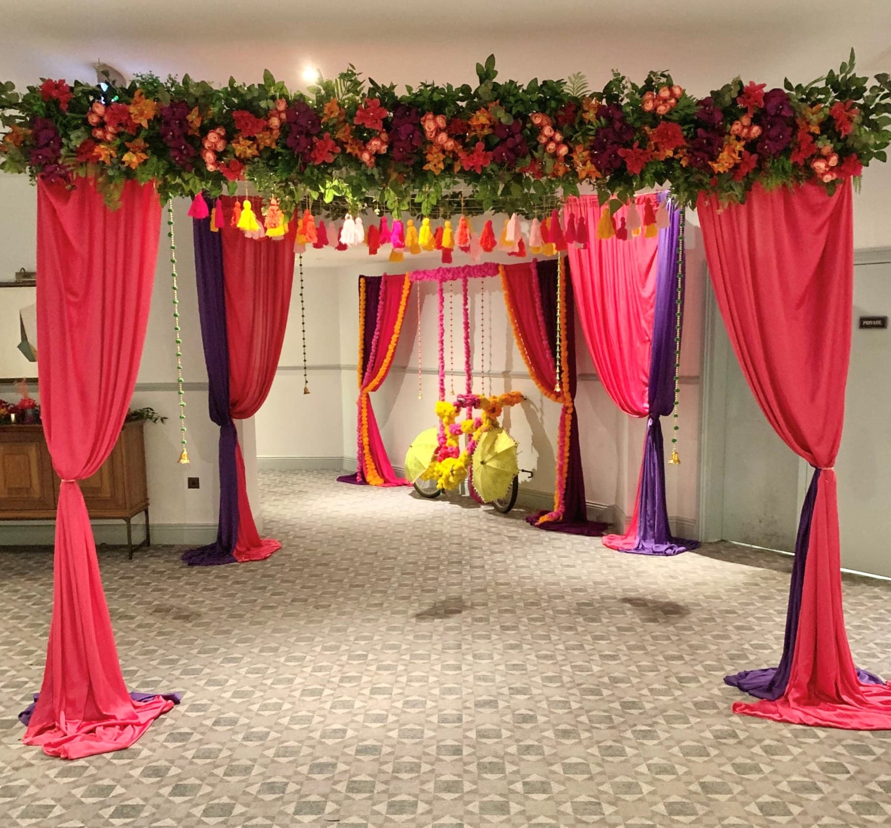 Pink and purple draped mandap with floral top and bright hanging tassels