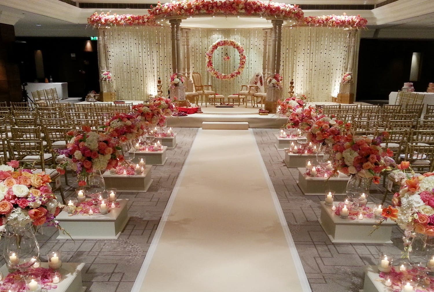 Long cream aisle with candle plinths leading to a round floral canopy mandap