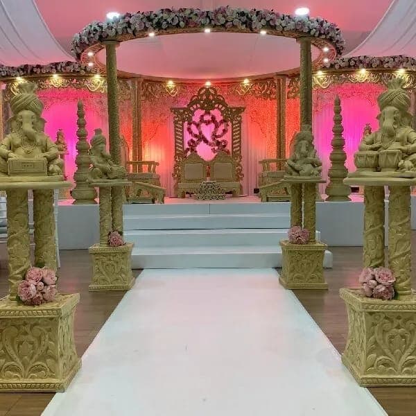 Carved Ganesh pedestals lining a white aisle to a magenta-lit stage mandap with a floral roof