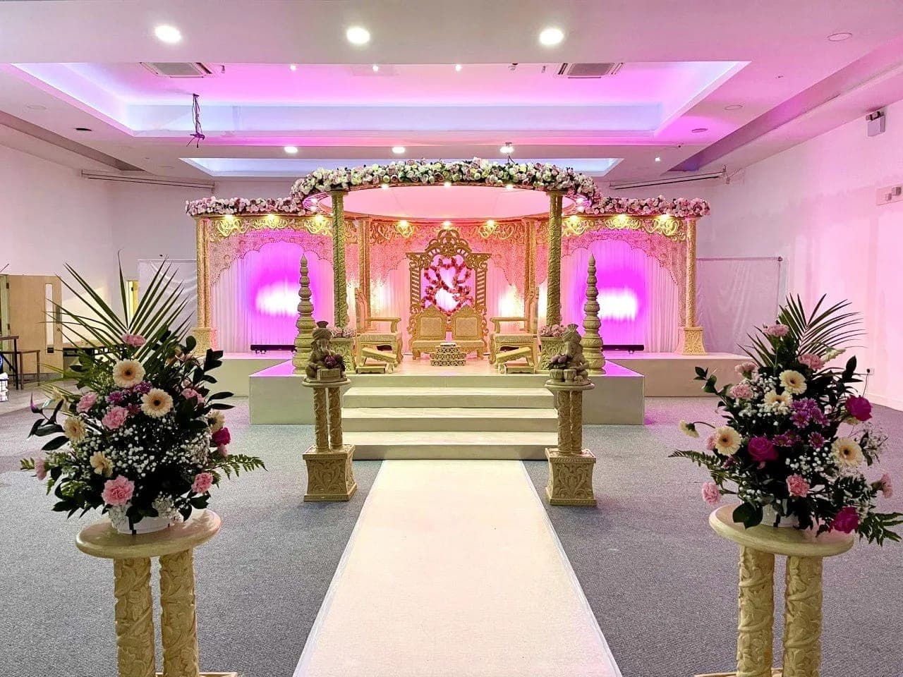 Cream and gold carved stage mandap with pink uplighting and heart motif down a white runner