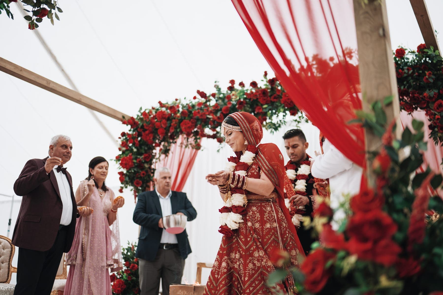 Timber framed mandap with red rose arch and red drape during a ceremony
