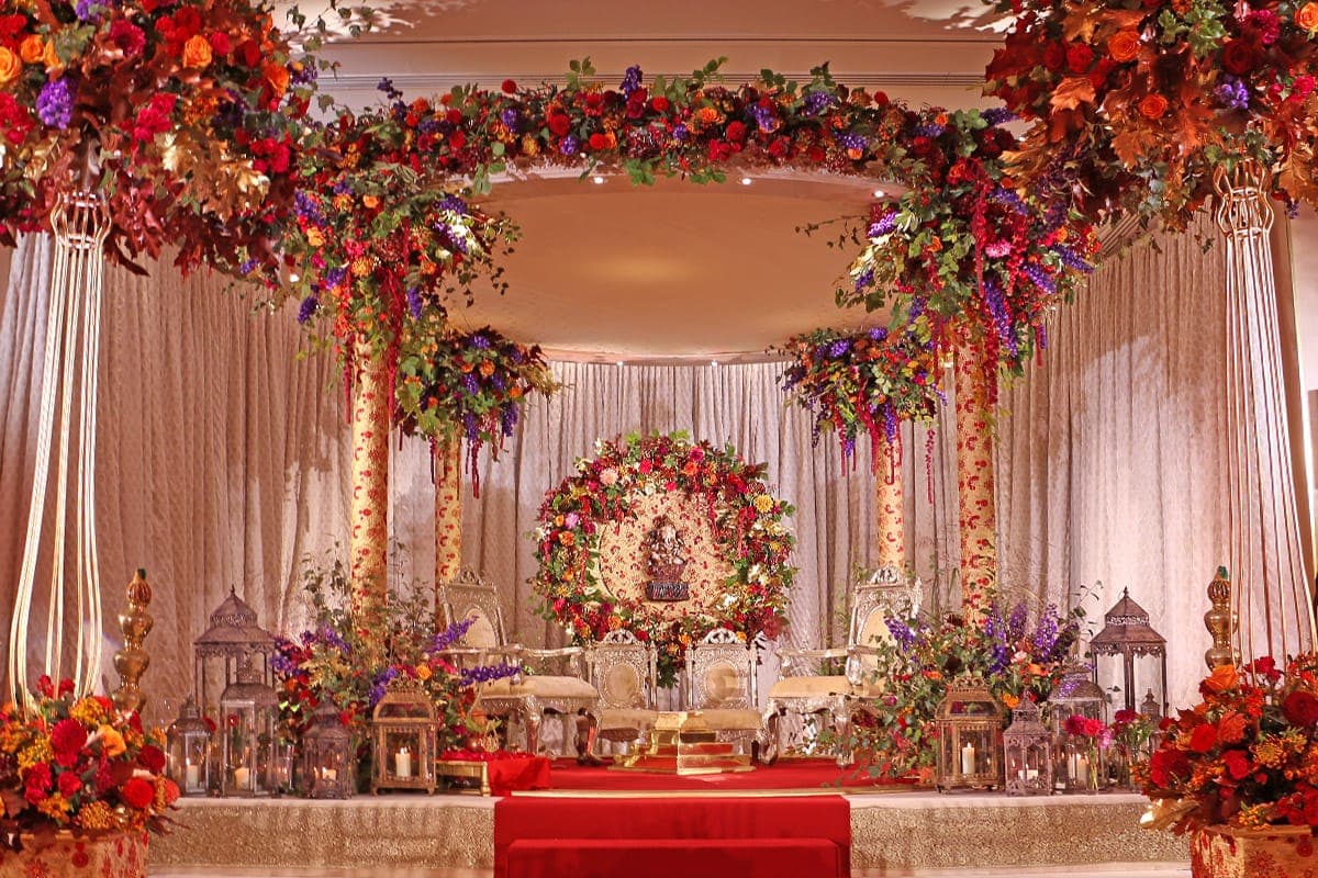 Tall flower-wrapped pillars with autumn blooms around a floral wreath and lantern-lined stage