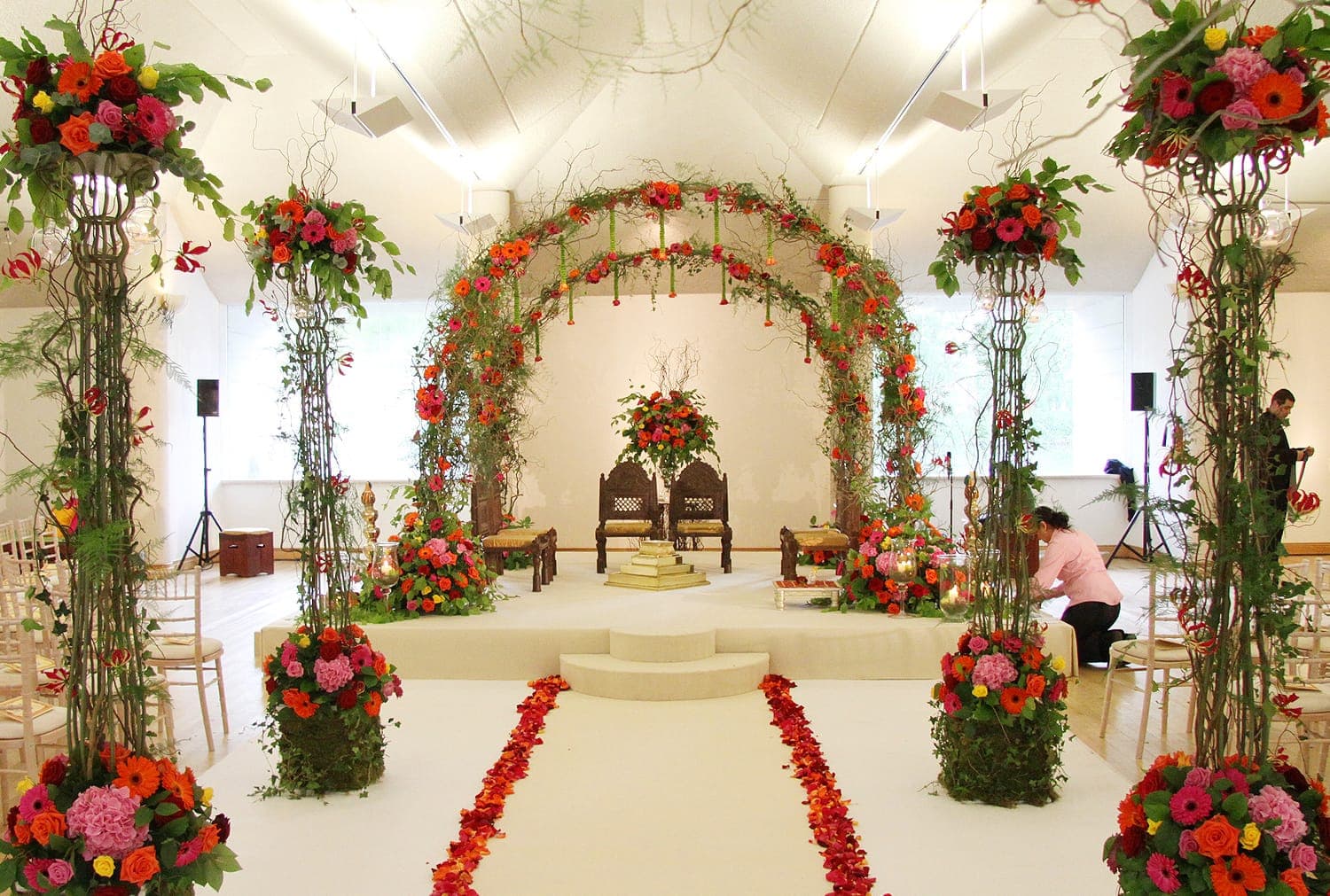 Orange gerbera twig arch with floral columns and petal aisle in a bright hall