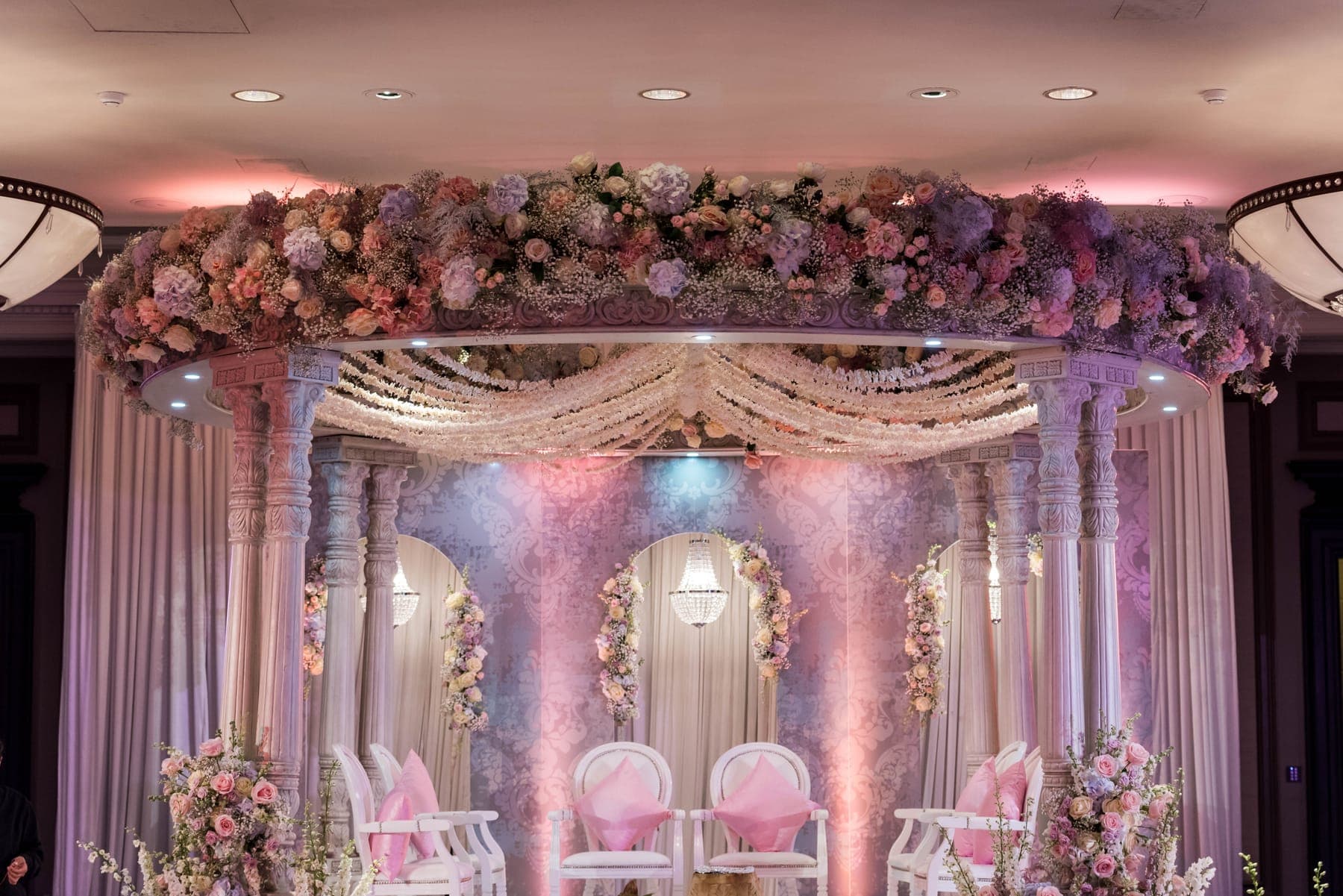 Pale carved columns and floral round roof under pink and violet lighting in a ballroom