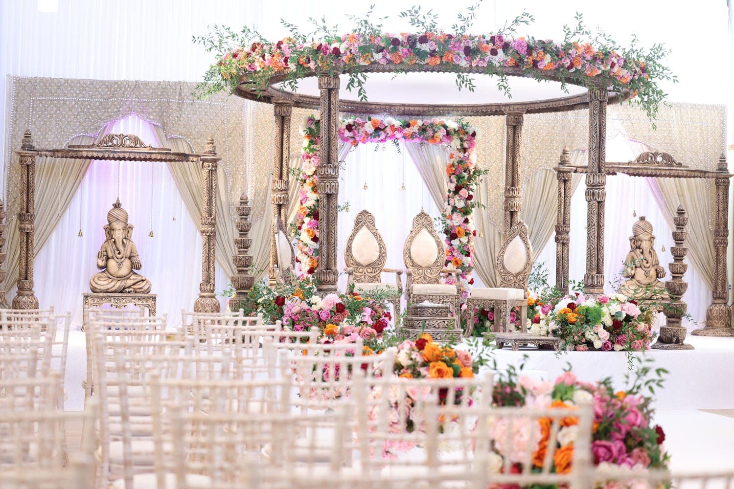 Bronze carved round mandap with orange and pink flowers and Ganesh side wings