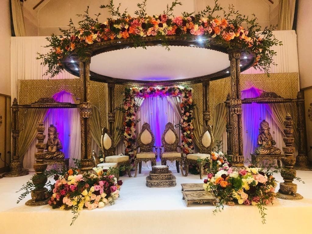 Round orange floral canopy over carved dark wood posts with statues and purple uplighting