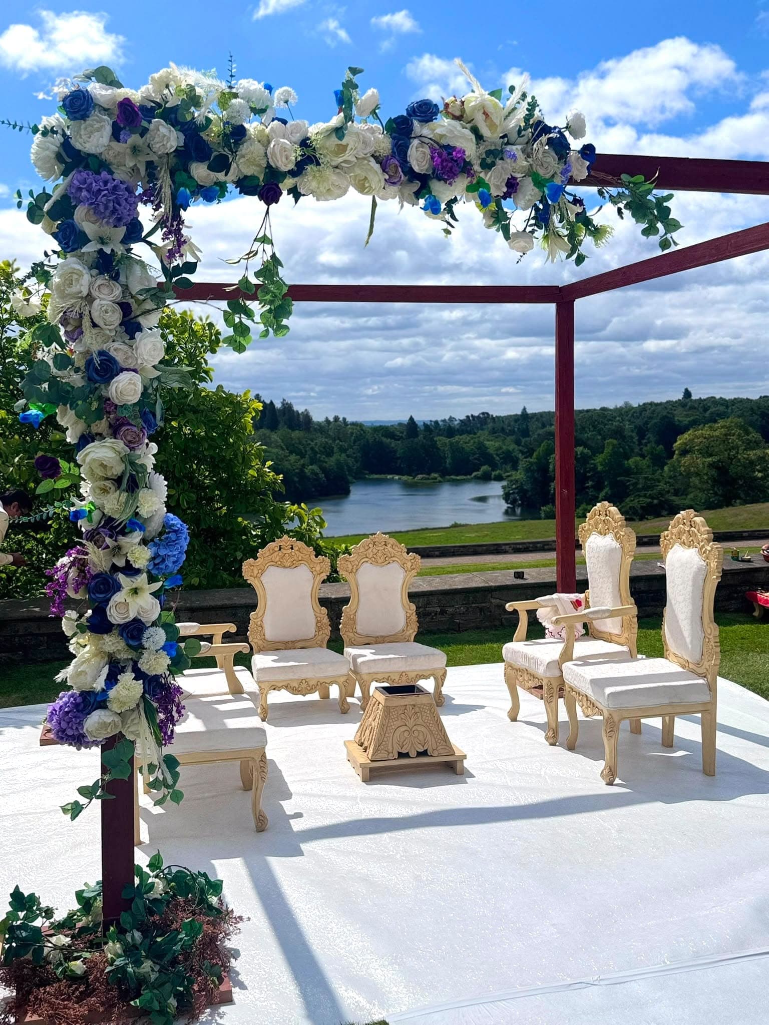 Dark red open frame with white, blue and purple florals on a white stage overlooking a lake