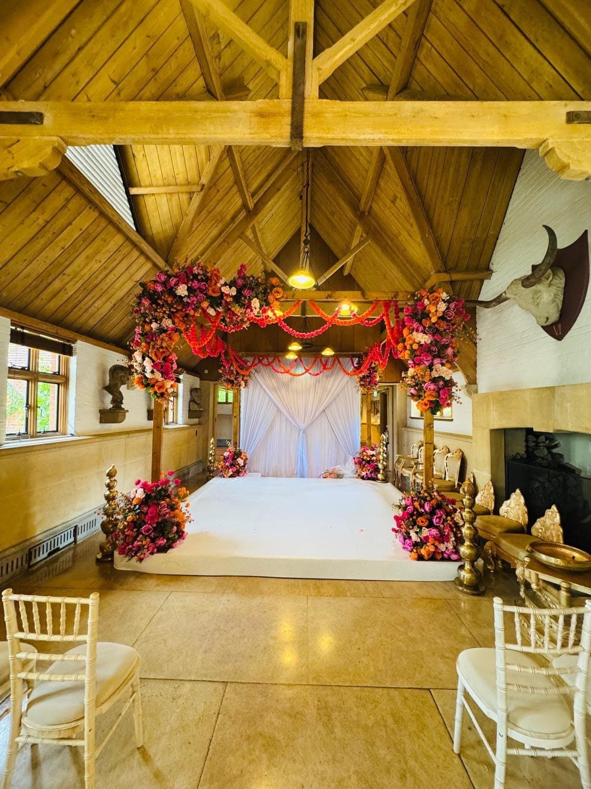 Aisle view toward the red floral mandap in a barn-style hall