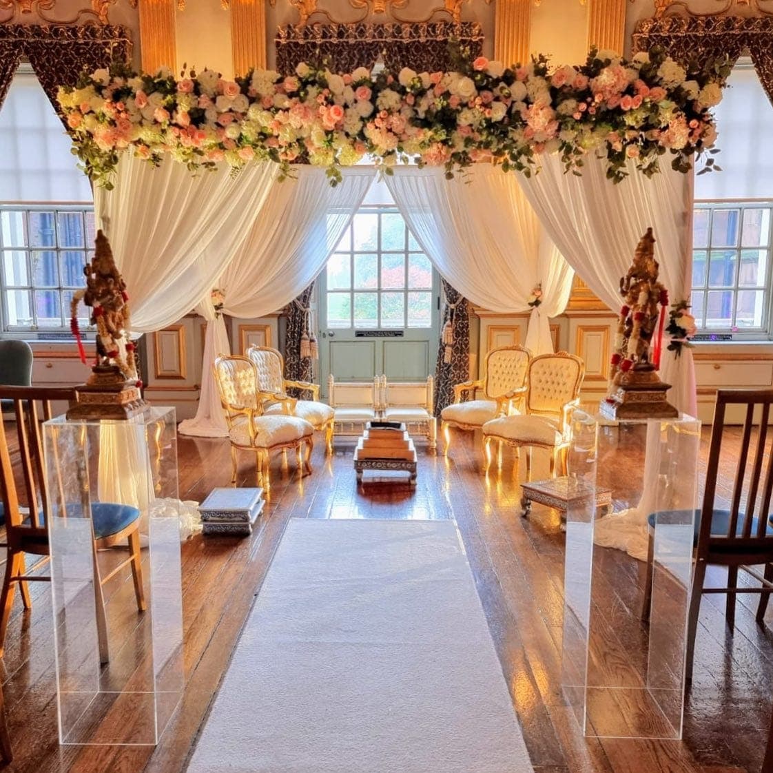 White draped mandap with peach rose beam in a panelled hall with wooden floor
