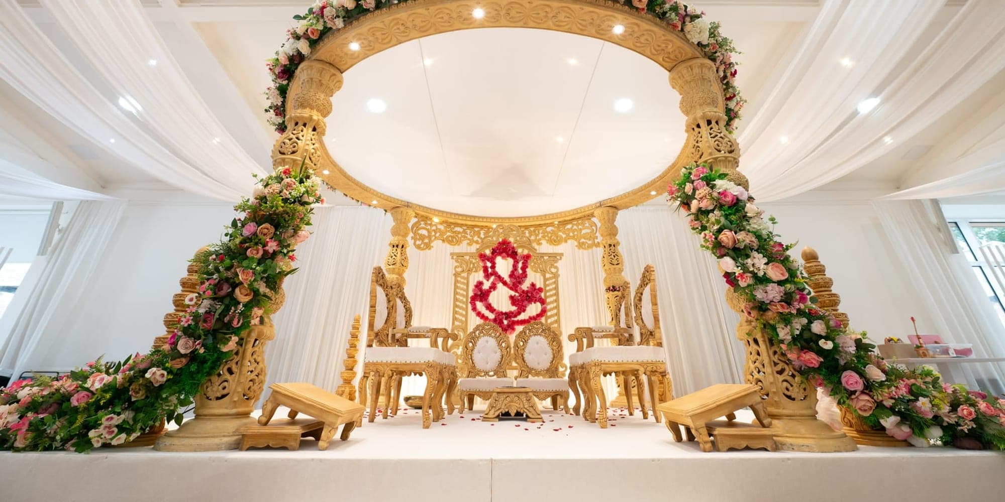 Accessible Wedding Mandap: Steps, Seating and Comfort Gold floral ring mandap with white drapes and a low stage with steps