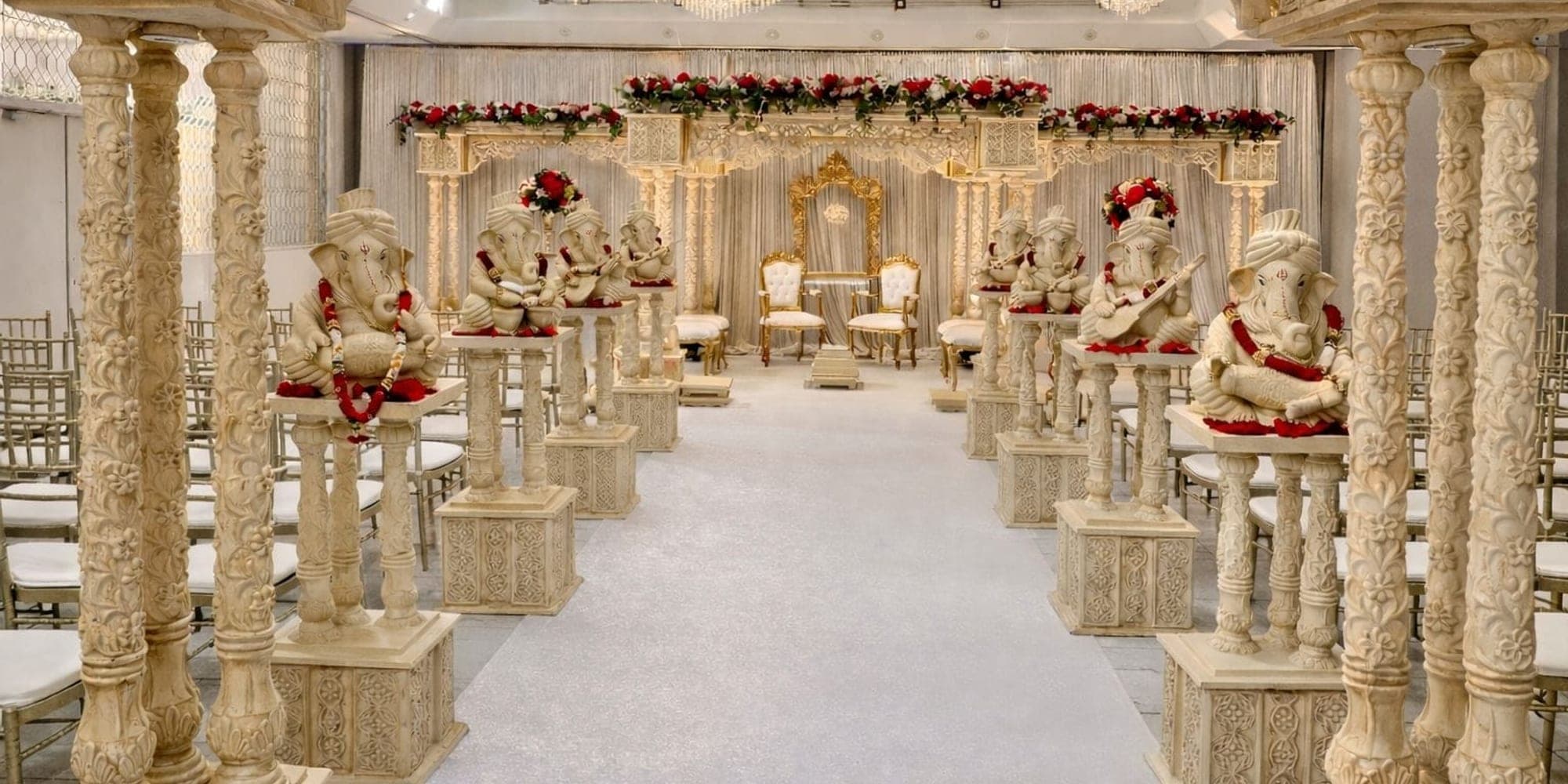 Getting the Best Value on Mandap Hire Carved ivory mandap with Ganesh statues on pedestals along a white aisle