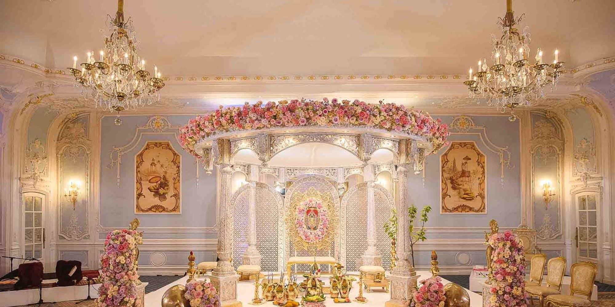 Mandap Lighting and Draping Ideas for Your Ceremony Ivory round canopy mandap under two chandeliers in a pale blue ballroom