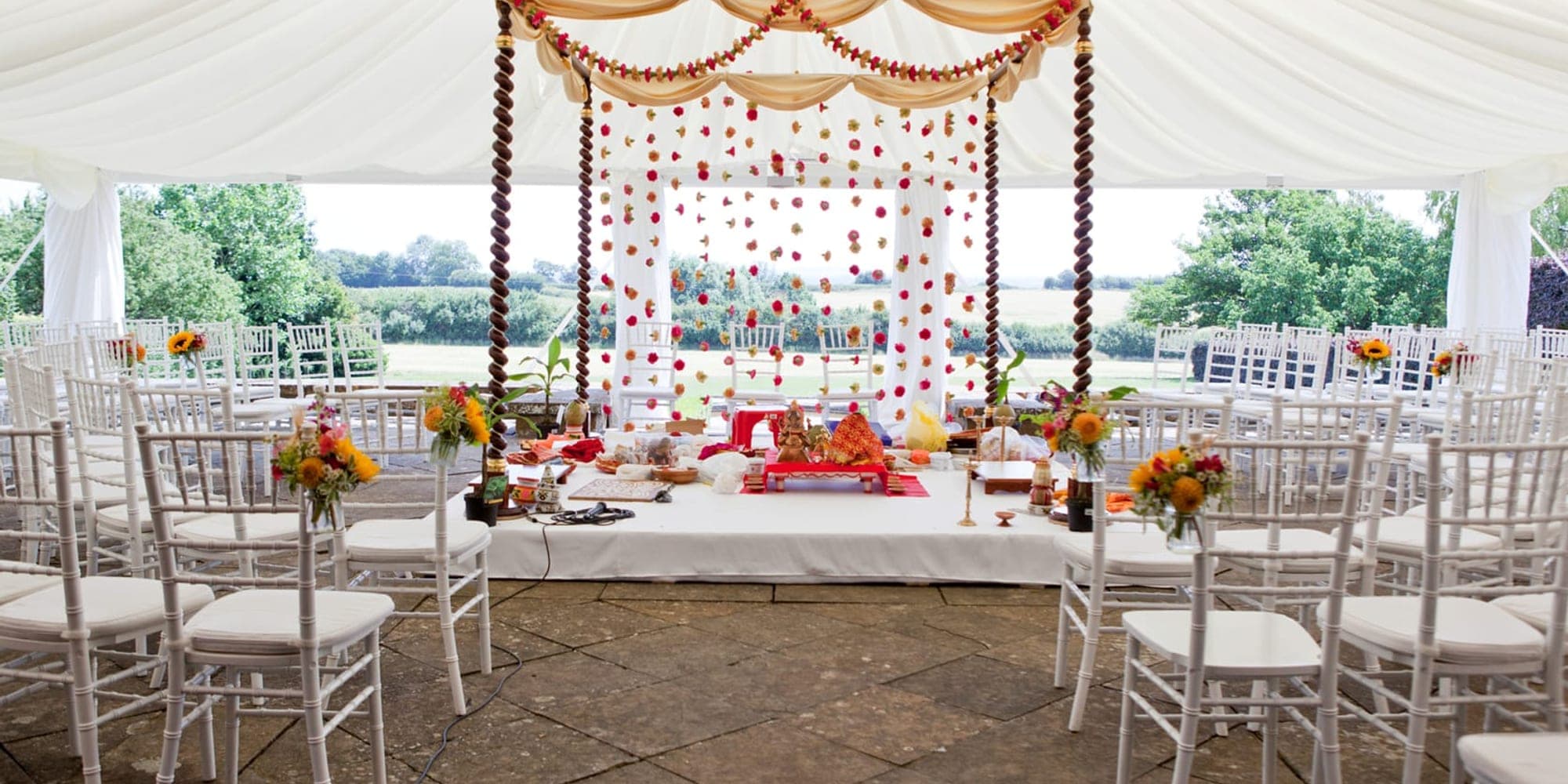 Mandap Hire for a Marquee: What to Check Before Booking White draped marquee with a garland-hung mandap and chairs overlooking a lawn