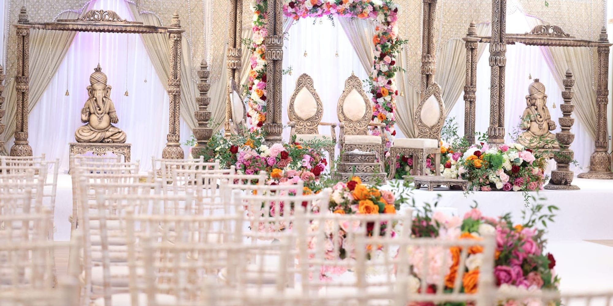 Mandap Structures Explained: Pillars, Canopies, Arches Round floral canopy mandap on pillars with a floral arch behind carved chairs