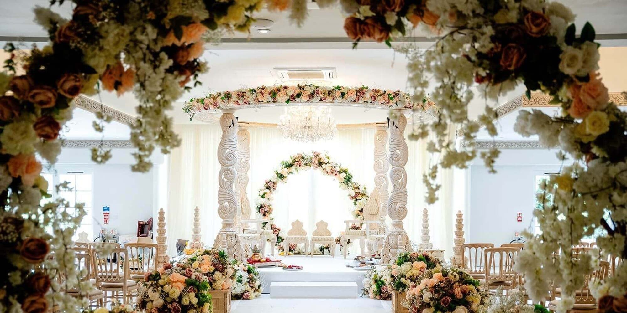 Mandap for Different Wedding Traditions: What Varies Floral tunnel framing a long white aisle toward a pillared mandap